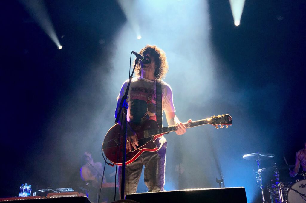 photo-of-singer-at-concert-onstage-with-guitar-and-blue-stage-lights-long-hair