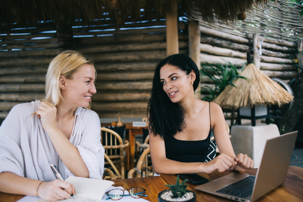 photo-of-friends-talking-with-each-other-while-working-on-projects-with-laptop-and-paper-diary-sitting-in-cafe