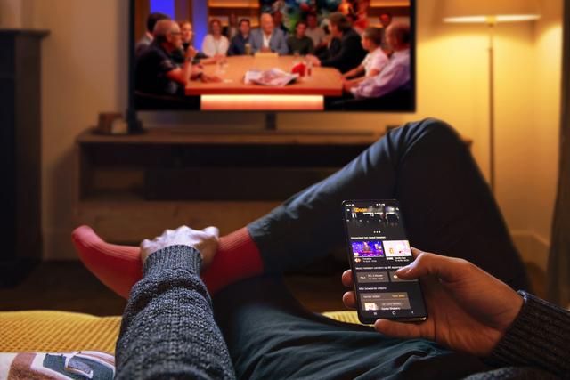 A girl sits in front of a TV with her phone, streaming services Ziggo Go Netherlands